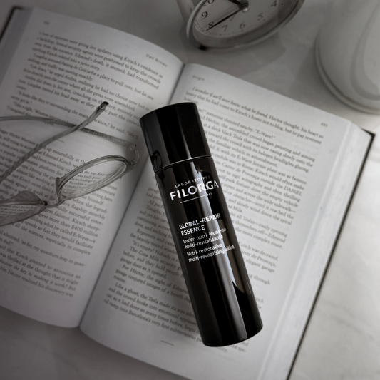GLOBAL-REPAIR ESSENCE and reading glasses laying on top of a book