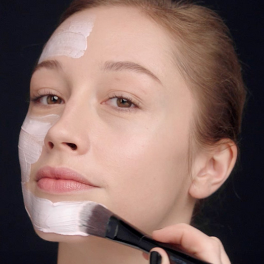 Woman applying exfoliating mask to her face with a brush