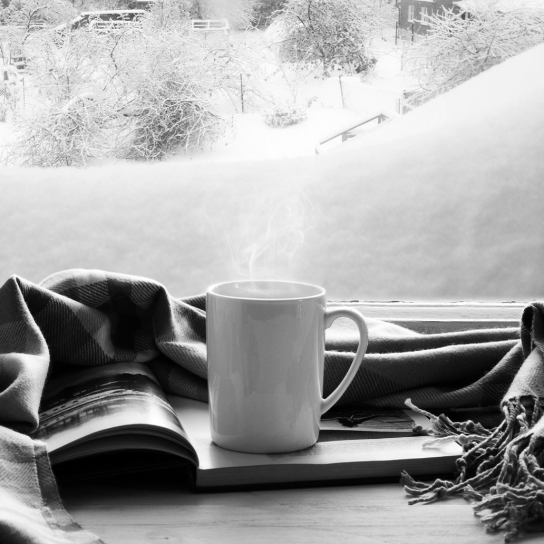 steaming beverage placed on top of magazine in front of window with a view of a snow-covered landscape