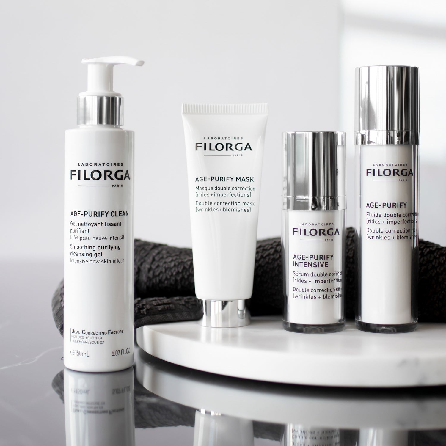 Full AGE-PURIFY COLLECTION on mirrored surface with black wash cloth behind products. 