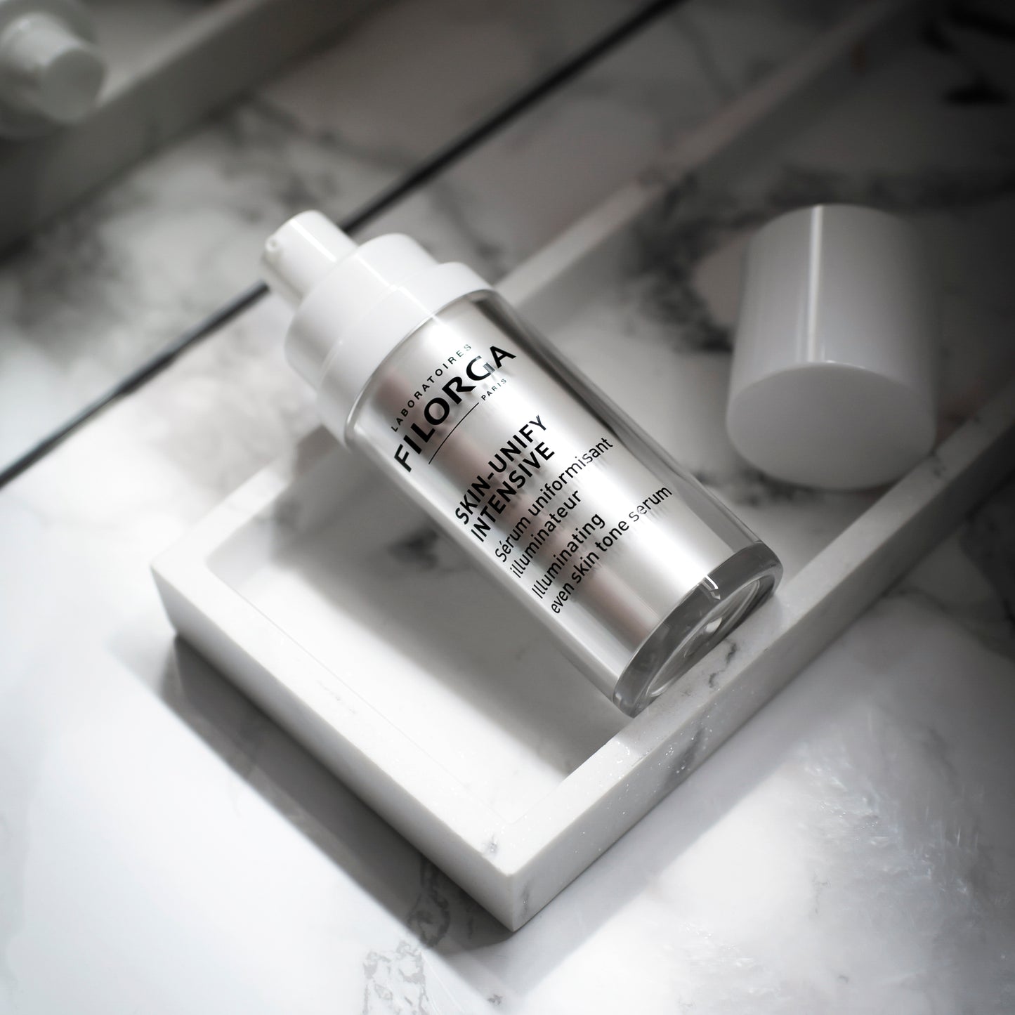 FILORGA SKIN-UNIFY INTENSIVE open bottle on its side on a white marble tray with black veins