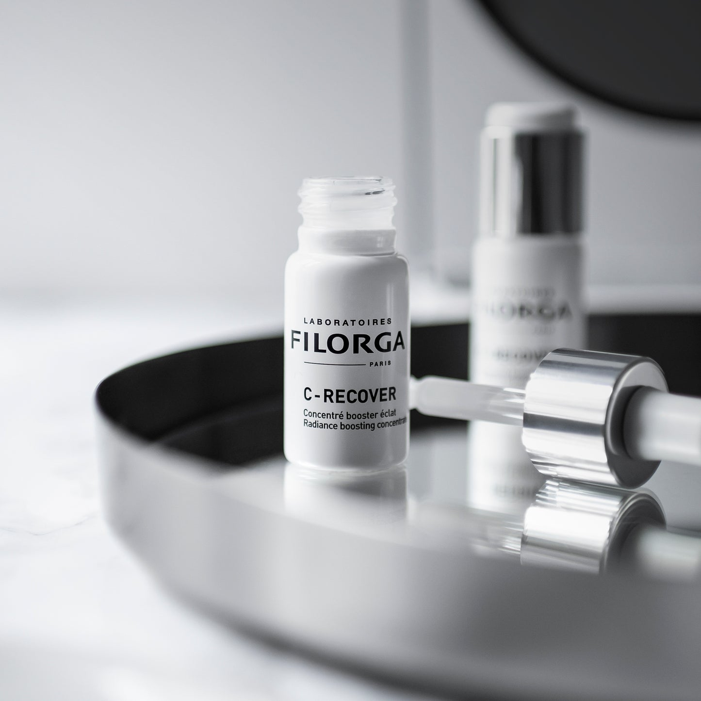 Open bottle of FILORGA C-RECOVER Concentrate and dropper on silver tray with other FILORGA products 