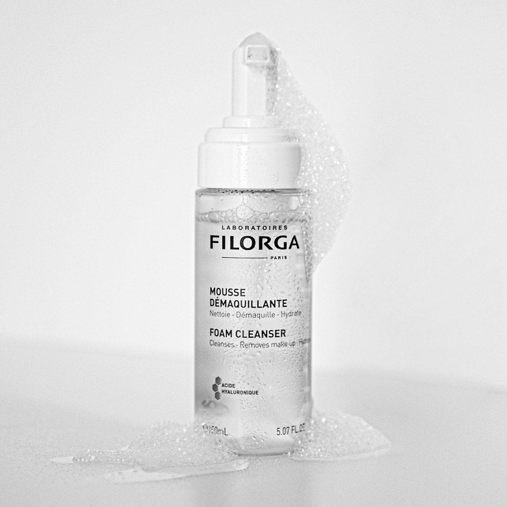 FILORGA FOAM CLEANSER open bottle with bubbles flowing out and down to a white countertop
